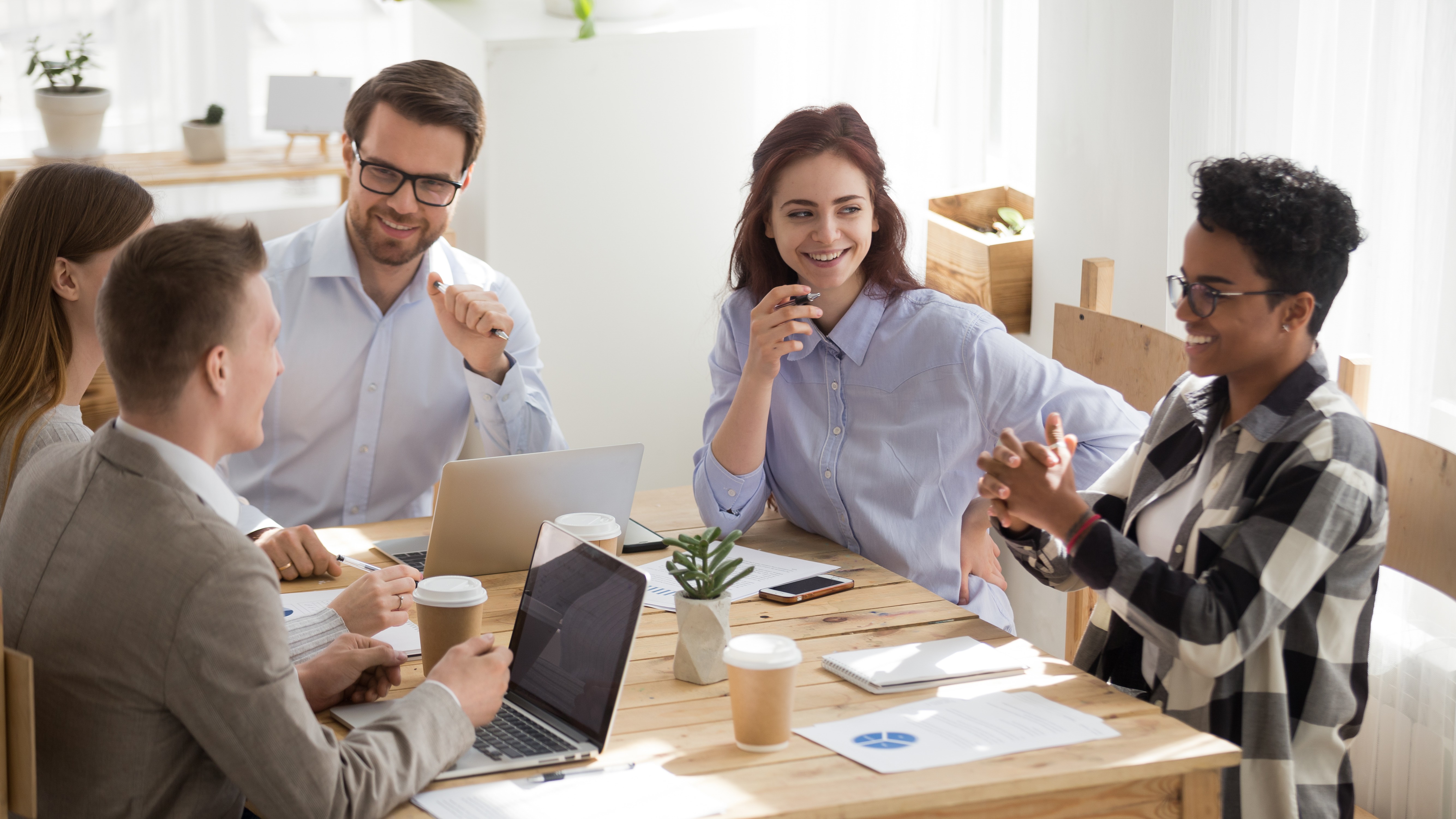 Five members sit around a table and have a good time in their workplace.